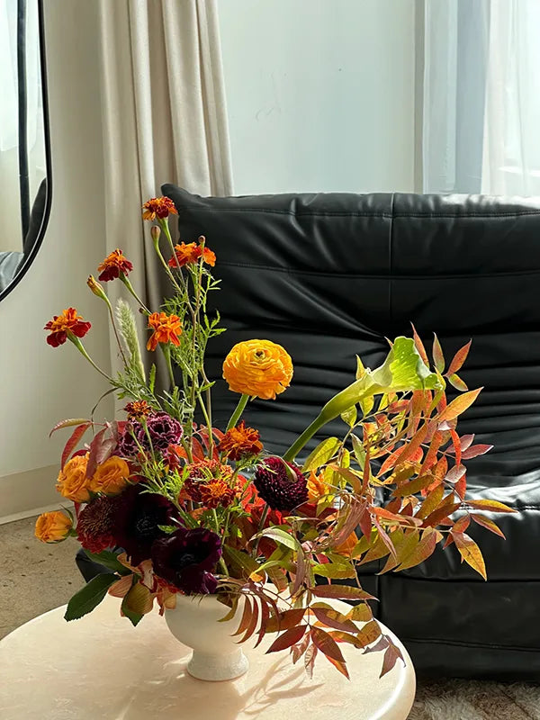 Autumn floral arrangement in white vase by black sofa